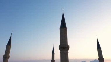 Kırmızı günbatımı gökyüzü arka planında dört cami minaresi.