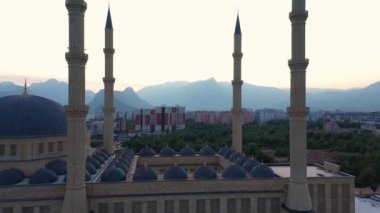 Dört minaresi olan güzel mavi bir cami. Şehir silueti ve arka planda dağlar.