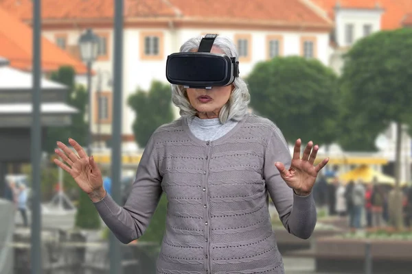 Překvapená zralá žena nosí brýle virtuální reality stojící na ulici. — Stock fotografie
