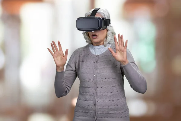 Ohromená starší žena s virtuální realitou sluchátka na abstraktním pozadí bokeh. — Stock fotografie