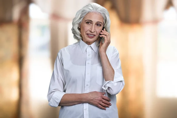 Красивая старшая деловая женщина разговаривает по мобильному телефону в помещении. — стоковое фото