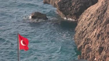 Sea waves hitting the rocks on the seaside. Turkish flag waving on wind.