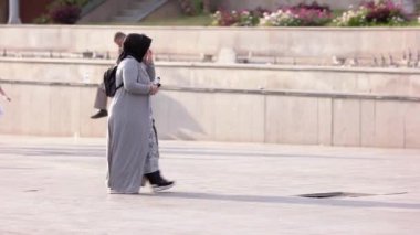 Olgun Müslüman kadın şehir caddesinde yürürken cep telefonunu kullanıyor..