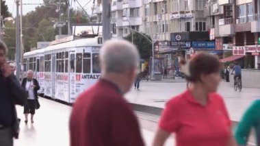 Kaldırımdaki caddede yürüyen yayalar. Trolleybus istasyona varır..