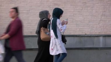 Genç Müslüman kadın şehir caddesinde arkadaşıyla yürürken akıllı telefon kullanıyor..