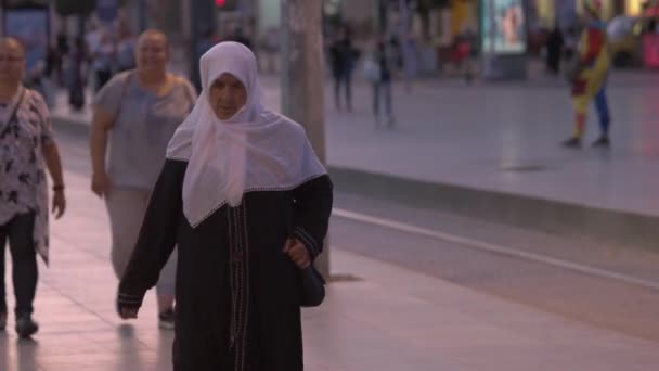 Senior Muslim woman in traditional hijab clothes walking alone on evening city street. — Stock Video