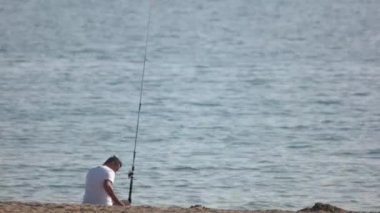 Adamın kumlu sahilde oturup balık tutuşu.