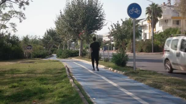 Vue arrière du jeune homme marchant sur une piste cyclable. — Video