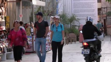 Turistler kaldırımlarda dükkan vitrinleriyle dar bir sokakta yürürler..
