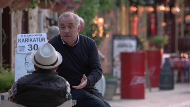 Två äldre män sitter och pratar utomhus. suddig stad gata bakgrund. — Stockvideo