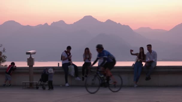 Langs de boulevard van de badplaats. Toeristen genieten van de prachtige zonsondergang boven zee en bergen. — Stockvideo