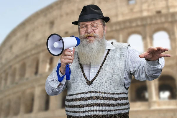 Starszy brodaty mężczyzna przemawiający do megafonu stojąc na niewyraźnym tle Koloseum w Rzymie, Włochy. — Zdjęcie stockowe