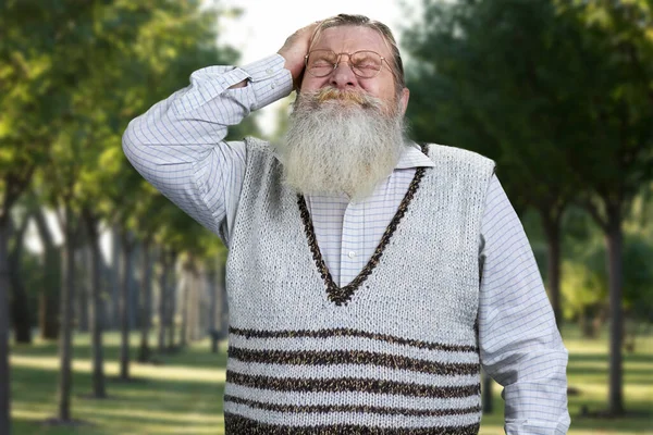 Oude man met baard die casual trui draagt en hoofd in de handen houdt en hoofdpijn of stress voelt. — Stockfoto