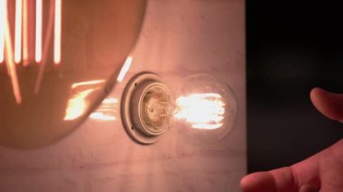 Close-up hand switches off light bulb on the wall.