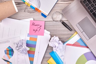 Sticky note with hurry up handwriting and office accessories.