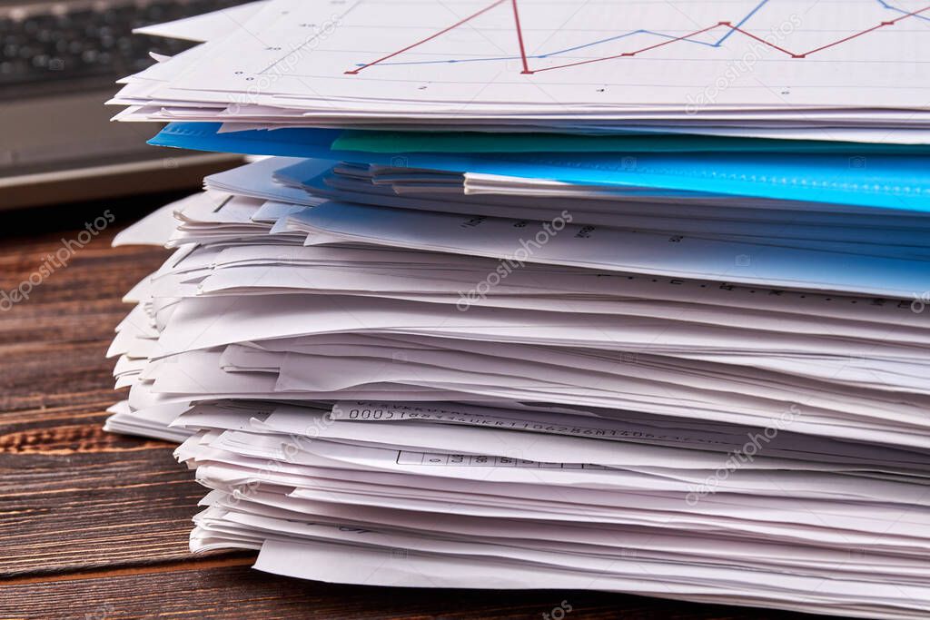 Close-up stack of office work papers on wooden desk.