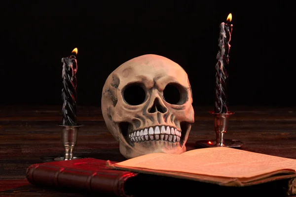 Satanische compositie van de menselijke schedel met satanisch boek en brandende kaarsen. — Stockfoto