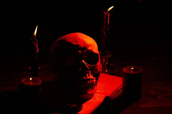 Mensen schedel en oranje licht van brandende kaarsen in het donker. — Stockfoto