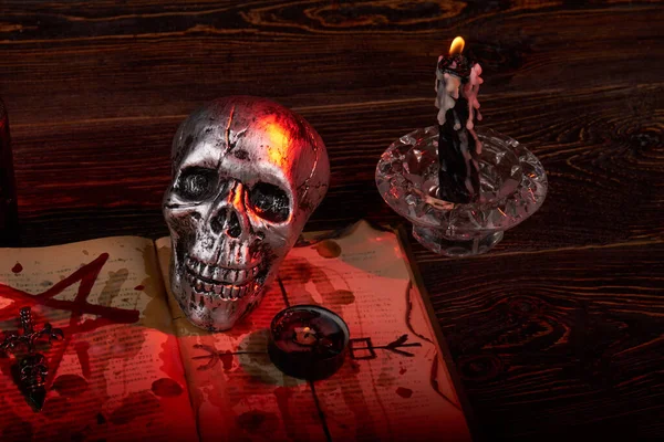 Metallic humans skull with candles and satanic bible with blood. — Stock Photo, Image