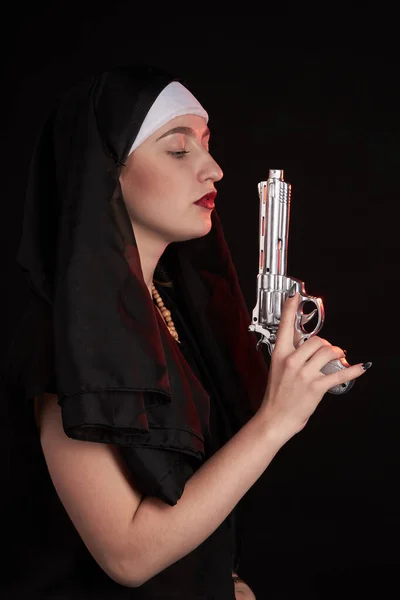 Jonge aantrekkelijke non draagt capuchon en houdt revolver pistool. — Stockfoto