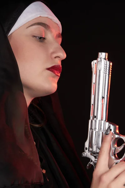 Zijaanzicht van een jonge sexy non met kap houdt zilveren pistool pistool. — Stockfoto