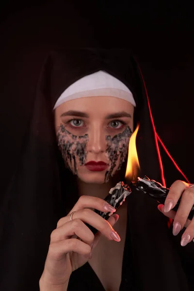Portré egy fiatal, hátborzongató gótikus lányról, aki tüzet gyújt két gyertya segítségével.. — Stock Fotó