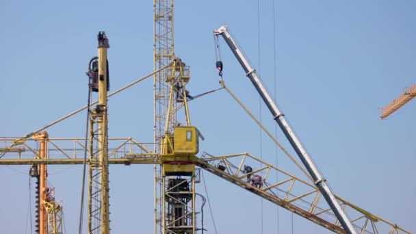 Los buliders de la construcción trabajan en las grúas sobre el fondo azul del cielo. — Vídeos de Stock