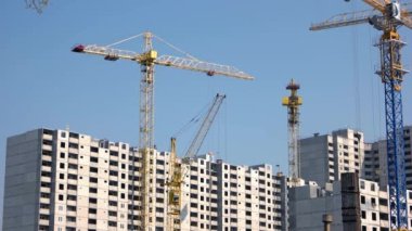 Mavi arka planda sarı turnalar ve yüksek binalar.