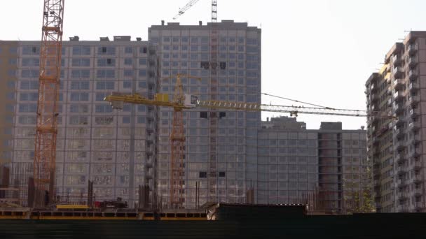 Žluté jeřáby a výškových budov na pozadí paprskové oblohy. — Stock video