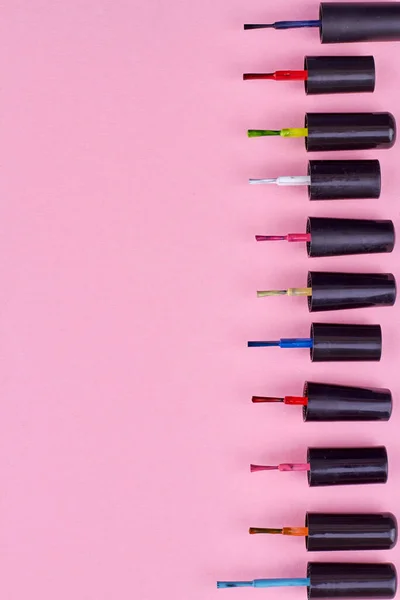 Row of colorful nail polishes brushes on pink background. Top view and copy space.