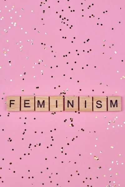 Wooden blocks with written text feminism on pink background. Top view and flat lay.