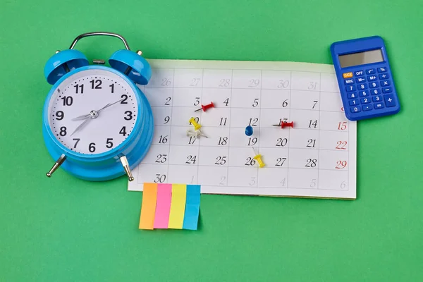 Time management and accounting concept top view flat lay. Calendar with alarm clock and calculator on green background.