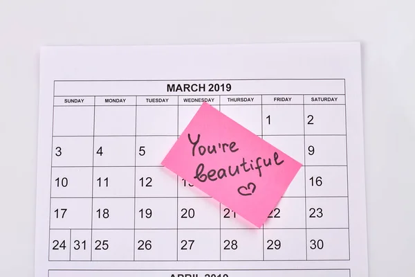 March calendar and sticker note with you are beautiful handwriting. Top view flat lay.
