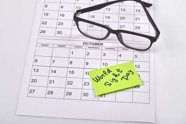 Glasses on the paper calendar and sticker note with handwriting. World sight day concept.