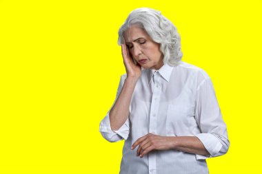 Sarı arka planda migrenden muzdarip stresli yaşlı kadın. Baş ağrısı ve sağlık sorunları kavramı.
