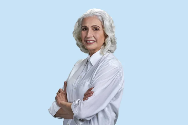 Mature business woman with crossed arms smiling and looking at camera. Cheerful business lady posing at camera on blue background.