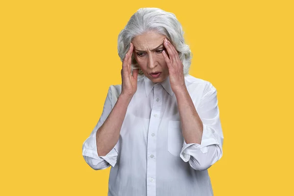 Unhappy elegant senior woman suffering from headache on color background. High blood pressure and stress concept.