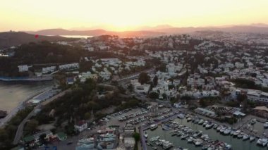 Tekneleri ve yatları olan deniz limanının havadan görüntüsü. Tatil köyü Bodrum. Şehrin ve dağların üzerinde gün batımı.