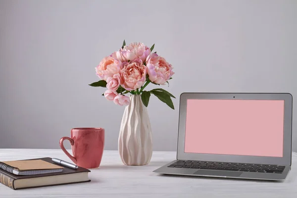 Vase of flowers with notepads and laptop with copy space. Notebook with pen and red cup.