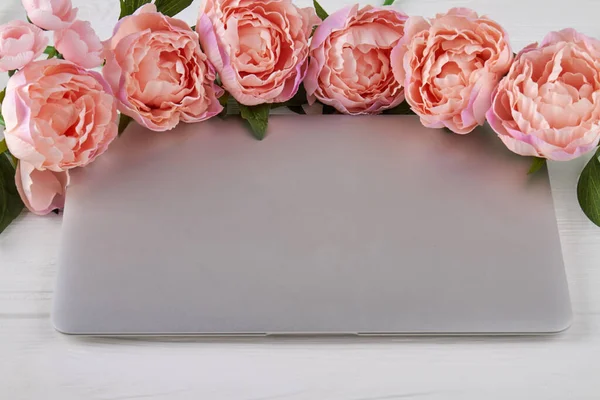Close up closed laptop with peony flowers. Home office desk workspace.