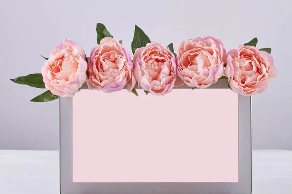 Laptop with blank screen decorated with pink flowers. Beautiful peonies on computer frame.