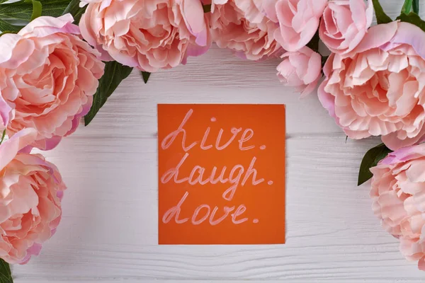 Peony flower frame and orange paper on white desk. Live laugh and love concept.