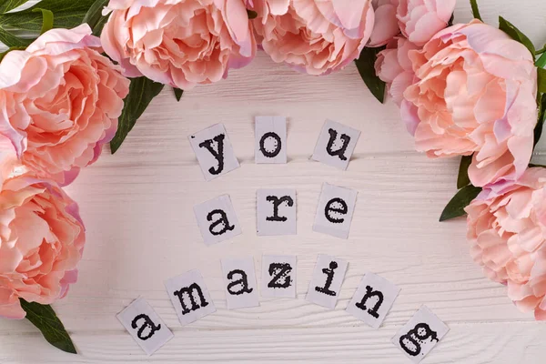 You are amazing inscription on white desk. Peony flowers frame.