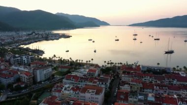 Aerial panoramic view of sea bay in Marmaris, Turkey. Top view of cityscape, seascape, boats anchored in the sea water and mountains in the background at sunset.