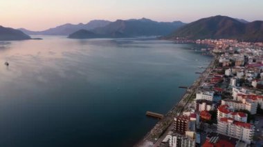 Picturesque sunset on sea bay. Embankment with city buildings, boats on sea water and mountains. Nature landscape from above.