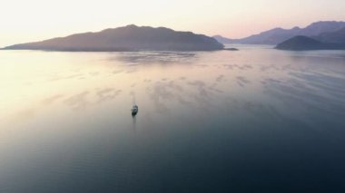 Aerial view of sea bay with lonely boat and mountains in the background. Beautiful seascape at sunset.