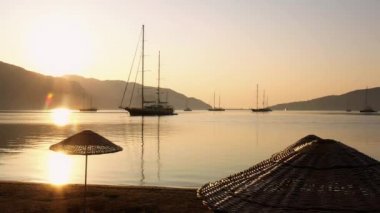 View of calm sea bay with boats in the morning. Sun rising over mountains. Sunrise sky in the background.