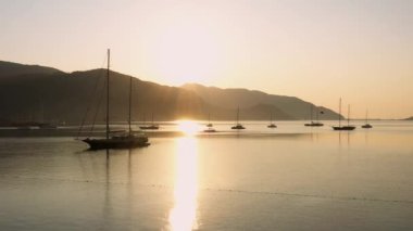 Calm sea bay with anchored yachts at sunrise. Mountains and morning sky in the background. Beautiful nature scene.