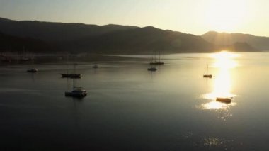 Many yachts parked in a bay of calm sea in the morning. Sun rising over mountains.