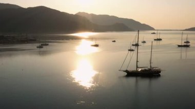 Aerial view of boats in sea bay. Sun reflection on water surface. Sunrise over sea and mountains. Go everywhere.